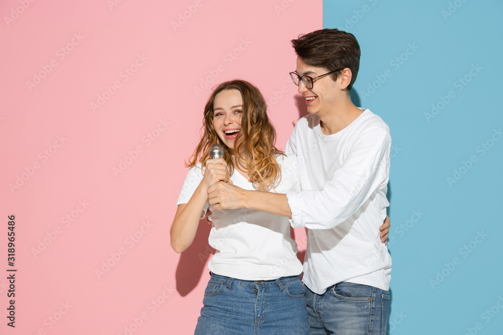 Singing song together. Young and happy man and woman in casual clothes on pink, blue bicolored background. Concept of human emotions, facial expession, relations, ad. Beautiful caucasian couple. Singing song together. Young and happy man and woman in casual clothes on pink, blue bicolored background. Concept of human emotions, facial expession, relations, ad. Beautiful caucasian couple.