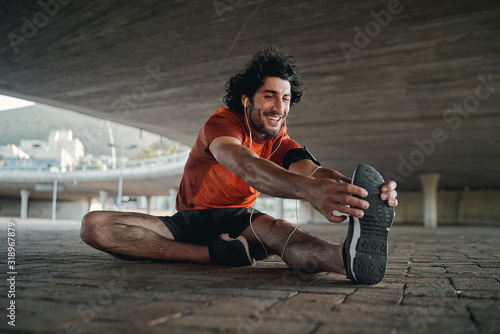 Smiling portrait of a fit young man sitting under the concrete bridge stretching his legs before running