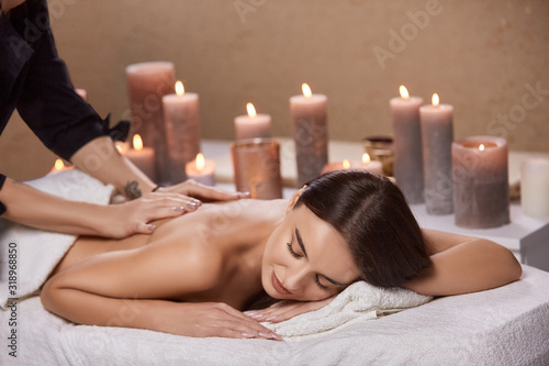 beautiful woman receiving massage and aroma theraphy with candles in beauty salon