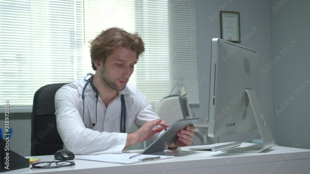 Doctor sit at a table in cabinet of hospital and work with tablet Doctor sit at a table in cabinet of hospital and work with tablet