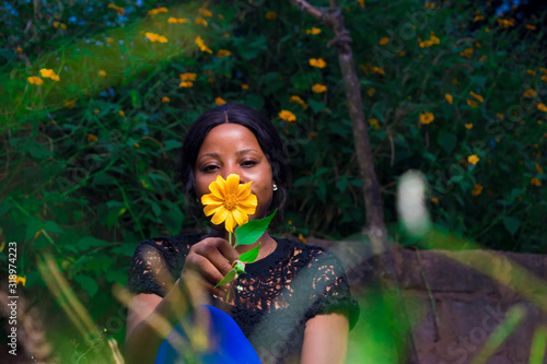 african girl holding a tree marigold flower sitting in a garden alone