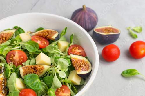 Fresh salad with figs, green leaves, cherry tomatoes and cheese on gray background. Free space for text. Top view. Abstract food background with big plate