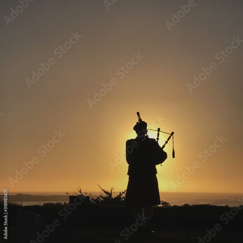 A silhouette of a bagpiper with the sun setting behind him and a view of the Pacific Ocean in Carmel, California