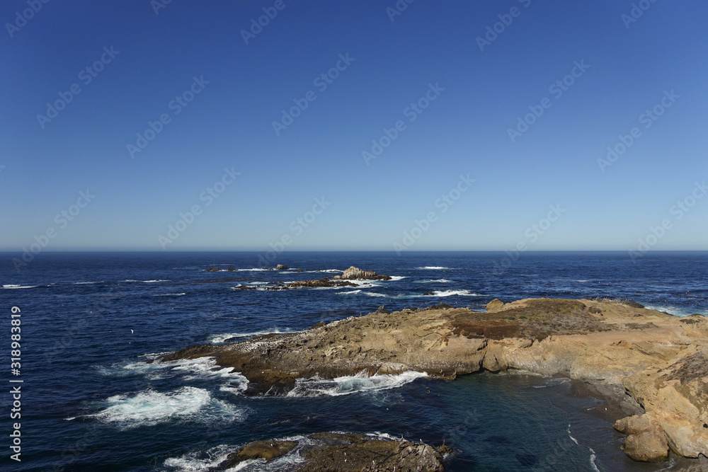 Looking out over the rocky coast of Big Sur and the blue Pacific Ocean under a clear blue sky; horizon