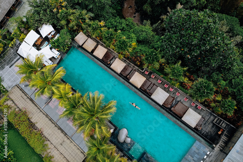 Aerial view of luxury pool with umbrellas and swimming around palm trees and jungle.Vacation concept. Drone photo