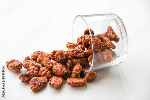 Sugar roasted pecan nuts (caramelized, praline nuts) in a glass on a white background, back view
