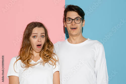 Shocked, astonished. Young and happy man and woman in casual clothes on pink, blue bicolored background. Concept of human emotions, facial expession, relations, ad. Beautiful caucasian couple.