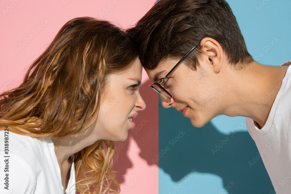 Angry face to face. Young and happy man and woman in casual clothes on pink, blue bicolored background. Concept of human emotions, facial expession, relations, ad. Beautiful caucasian couple. Angry face to face. Young and happy man and woman in casual clothes on pink, blue bicolored background. Concept of human emotions, facial expession, relations, ad. Beautiful caucasian couple.