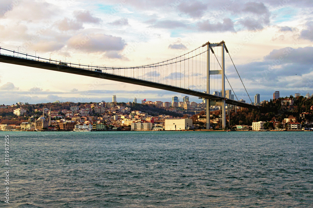 Beautiful landscape view of Bosphorus Bridge (also known as 15 July Martyrs Bridge) over strait. Beylerbeyi district with Beylerbeyi Mosque in the background. Winter sunny day. Istanbul, Turkey