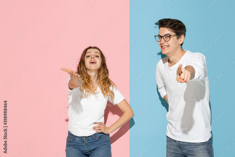 Pointing on, choosing. Young and happy man and woman in casual clothes on pink, blue bicolored background. Concept of human emotions, facial expession, relations, ad. Beautiful caucasian couple. Pointing on, choosing. Young and happy man and woman in casual clothes on pink, blue bicolored background. Concept of human emotions, facial expession, relations, ad. Beautiful caucasian couple.