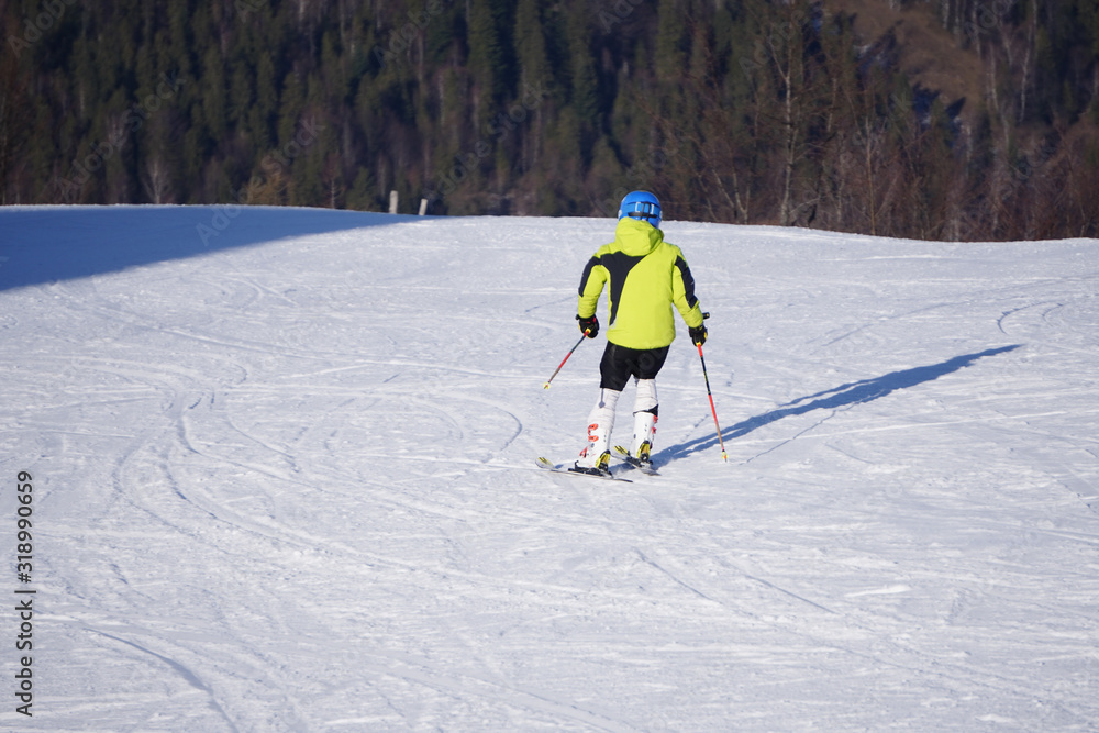 One person in bright clothes goes downhill on skis at a ski resort. Winter recreation, sports or training time. Person goes down the mountain