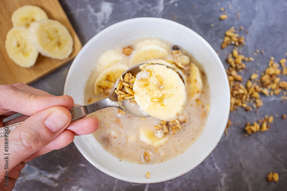 Muesli with chocolate and fresh banana on a dark gray marble table. Hand holds a spoon over a plate. Nearby are bananas on a wooden cutting board. The concept of healthy food, healthy breakfast. Muesli with chocolate and fresh banana on a dark gray marble table. Hand holds a spoon over a plate. Nearby are bananas on a wooden cutting board. The concept of healthy food, healthy breakfast.