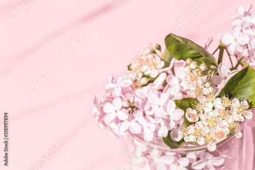 Fototapeta Naklejka Na Ścianę i Meble -  Assorted lilac and spring flowers in bloom in glass vase on pink background with copy space and shadow. Birthday celebration or wedding invitation card. Spring summer concept.