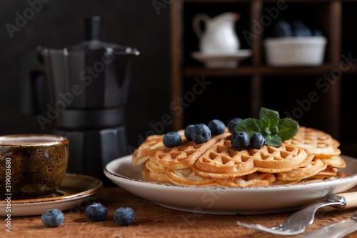 Close-up of soft Viennese waffles with blueberries, a cup of coffee and a coffee pot