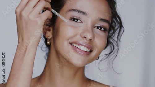 beautiful female using face oil with pipette and moisturizing her cheeks