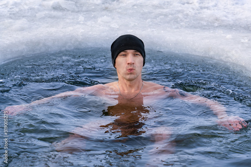 A man in a hat plunges into ice water in winter and takes his breath away