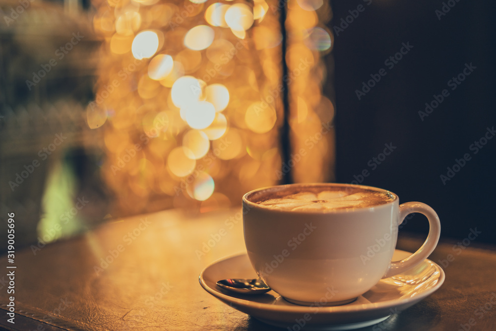 Obraz premium A white cup of coffee with spoon and saucer on a wooden table and luxury vintage. a blur of bokeh 