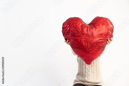 Young female in white sweater hide her face behinde big red heart isolated over white background, copyspace