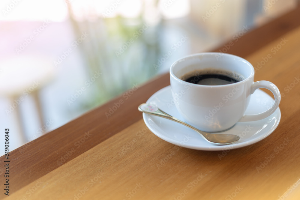 The white ceramic coffee cup with coaster is placed on a brown wooden base on the back, naturally a blurred background. The white ceramic coffee cup with coaster is placed on a brown wooden base on the back, naturally a blurred background.