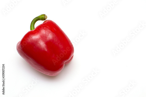 One bright red raw bell pepper with green tail on a white isolated background with a place for recording