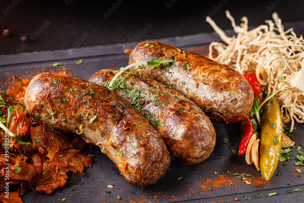 German cuisine. Pork and beef sausages, with spices, vegetables and cabbage. Modern serving dish in a restaurant on black slate. background image, copy space text