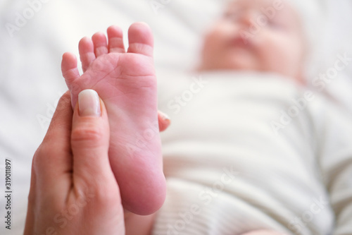 Massage. Close up baby feet in mother hands. Copyspace. Young caucasian woman makes massage for happy infant baby on white bed at home © Наталия Кузина