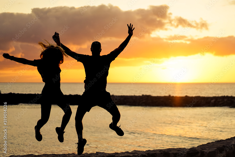 Fototapeta premium Silhouette of friends jumping in sunset. Silhouette of couple near ocean water. Holidays, relationship and love concept. Original sunset color - Image