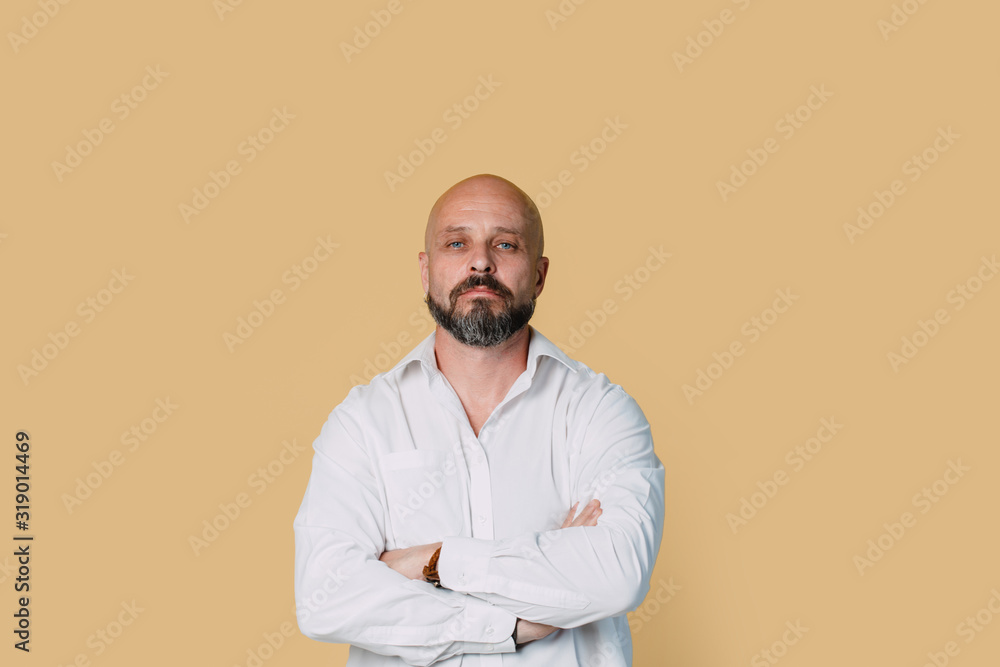 Serious middle-aged man with folded arms and a deadpan expression posing in front of a beige background with copy space Serious middle-aged man with folded arms and a deadpan expression posing in front of a beige background with copy space