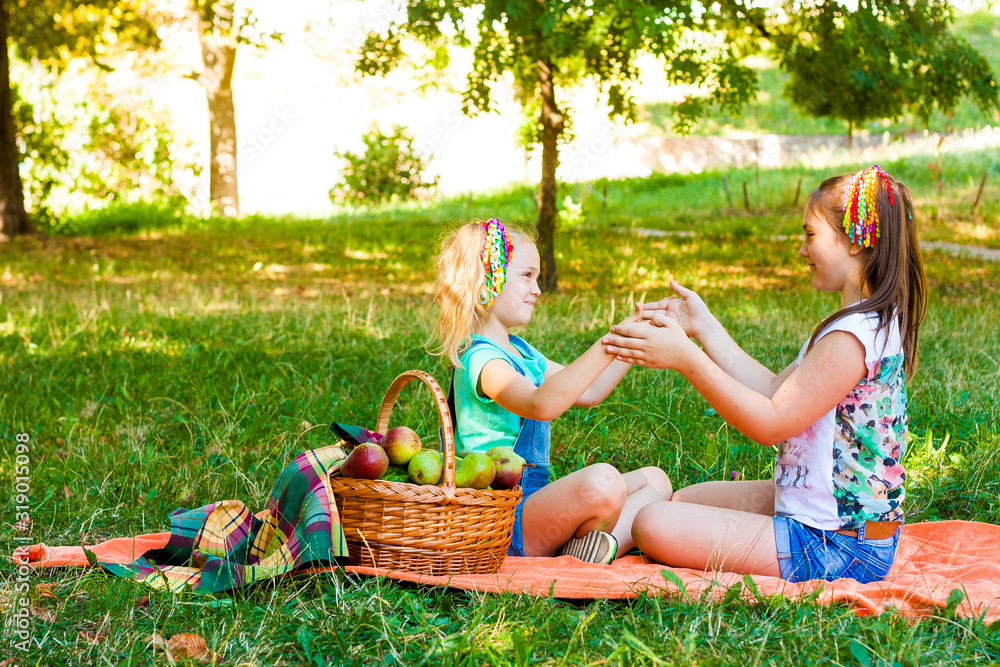 Two Girls Play On Orange Picnic Blanket With Picnic Basket In The Park