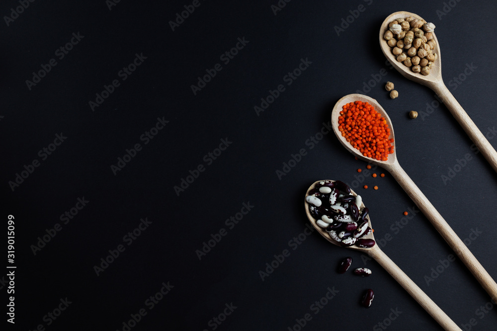Lentils chickpeas and beans on a dark background in wooden spoons Lentils chickpeas and beans on a dark background in wooden spoons