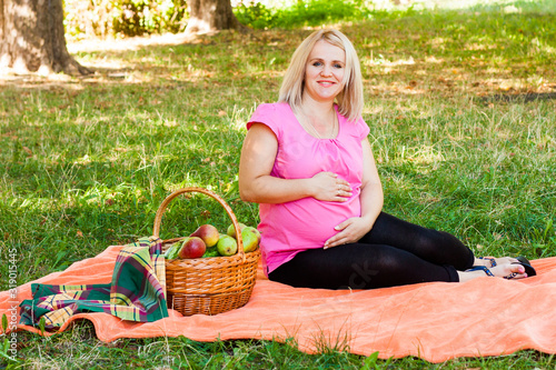 Obraz na płótnie Happy Pregnant Woman Sits On Orange Picnic Blanket With Picnic Basket In The Park w salonie