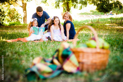 Obraz na płótnie Happy Two Parent Family With Two Daughters On Orange Picnic Blanket In The Park. Picnic basket in bokeh w salonie