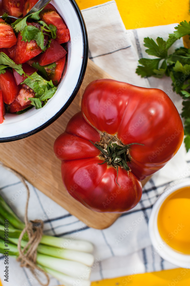 Giant fleshy ripe red tomato on a wooden Board, tomato and green salad in a plate. Vegetable menu, vegetarian menu. Giant fleshy ripe red tomato on a wooden Board, tomato and green salad in a plate. Vegetable menu, vegetarian menu.