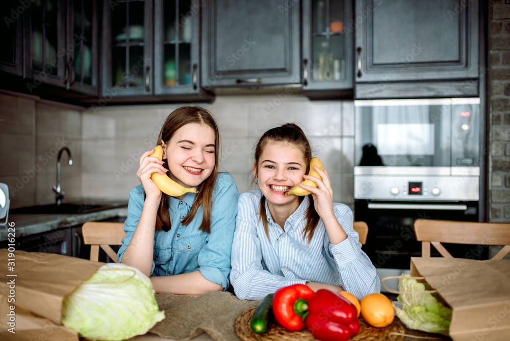 Two funny girlfriends in the kitchen. Fresh vegetables, healthy nutrition. Red pepper and apples, fresh green Beijing cabbage in a craft package. eco food packaging Two funny girlfriends in the kitchen. Fresh vegetables, healthy nutrition. Red pepper and apples, fresh green Beijing cabbage in a craft package. eco food packaging