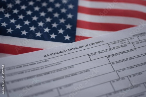 U.S. standard certificate of live birth application form next to flag of USA. Birthright citizenship concept.