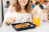 Girl eating sushi with chopsticks while having Bento lunch in the food court