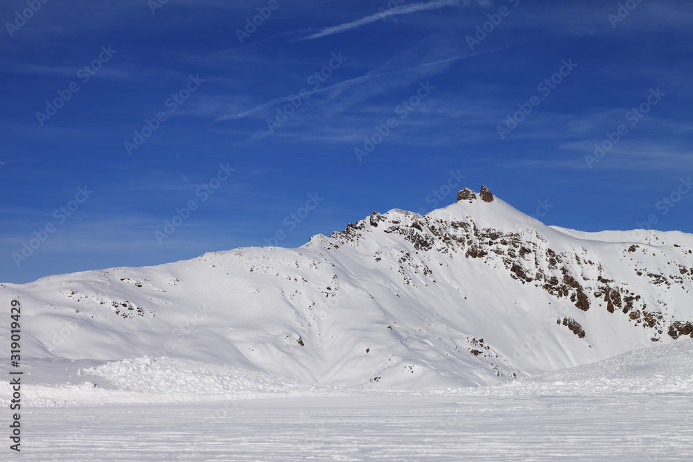 Snowy ski slope at high winter mountains and sunlit blue sky