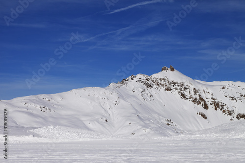 Snowy ski slope at high winter mountains and sunlit blue sky