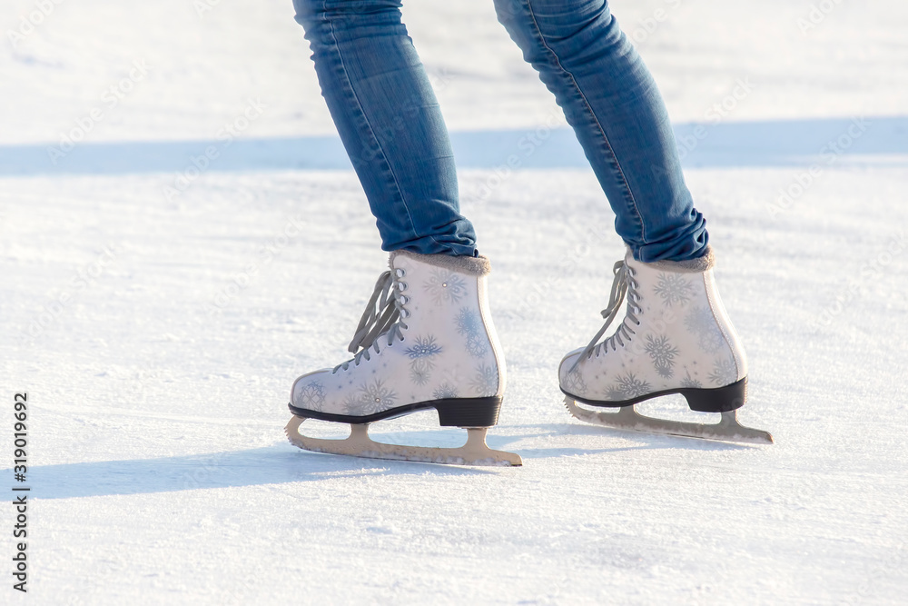 legs of a girl in blue jeans and white skates on an ice rink. hobbies and leisure. winter sports legs of a girl in blue jeans and white skates on an ice rink. hobbies and leisure. winter sports
