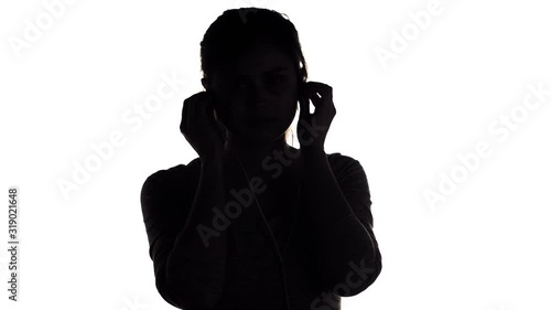 silhouette of a young happy woman listening to music in big headphones and holding a smartphone, girl relaxing on white isolated background, concept lifestyle