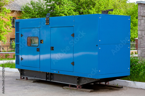 Diesel generator for emergency power supply at the wall of a medical center against the backdrop of green trees in fine weather.