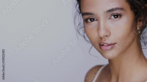 pretty girl with black hair fixed behind, big eyes, thick eyebrows and naked shoulders at gray background, copy space, beauty photo, close up.