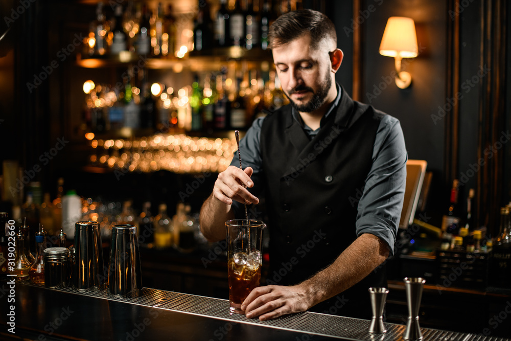 Male bartender stirring alcohol cocktail with bar spoon