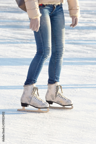legs of a girl in blue jeans and white skates on an ice rink. hobbies and leisure. winter sports