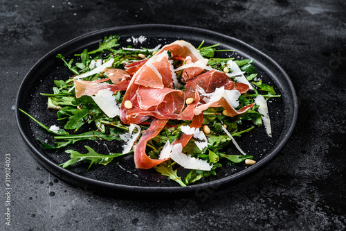 Salad with Serrano jamon, ham, rucola and Parmesan cheese. Black background, top view.