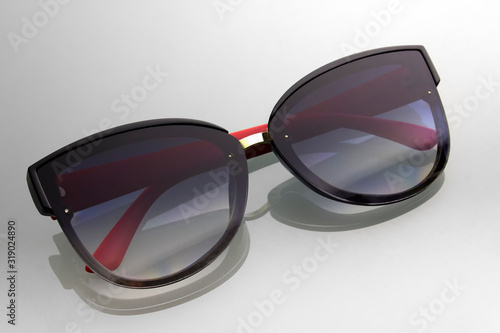 Sunglasses on a background of gray gradient with shadow reflection. Black glasses with red ears. Accessory for relaxation and walking on sunny days.