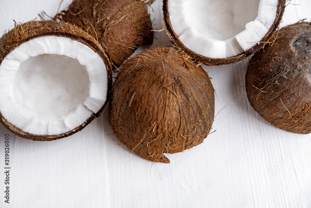 Close-up of a broken coconut fruit on a white wooden background with a place for inscription. Banner for spa center, healthy diet, coconut oil for food and body.