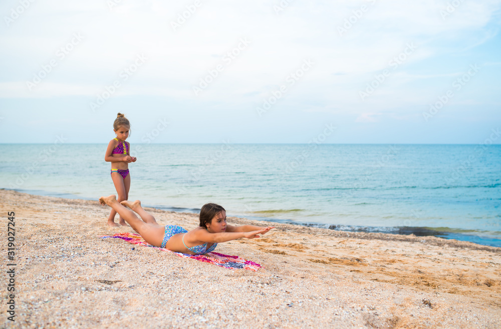 Charming little girls do gymnastic exercises while relaxing on the beach on a sunny warm summer day. The concept of sports and active games in the summer. Copyspace