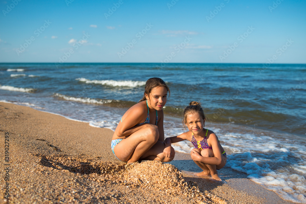 Two cute little little sisters play in the sand on the beach on a sunny summer day. Family vacation concept with children. Copyspace Two cute little little sisters play in the sand on the beach on a sunny summer day. Family vacation concept with children. Copyspace
