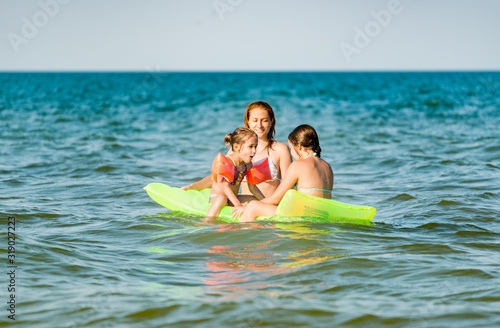 Rear view of a positive young family mom and two little daughters swim on a yellow air mattress in the sea on a sunny summer day during vacation. Relaxation concept. Copyspace © YouraPechkin